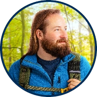 Right-facing profile of adult male hiker with backpack against forestland background
